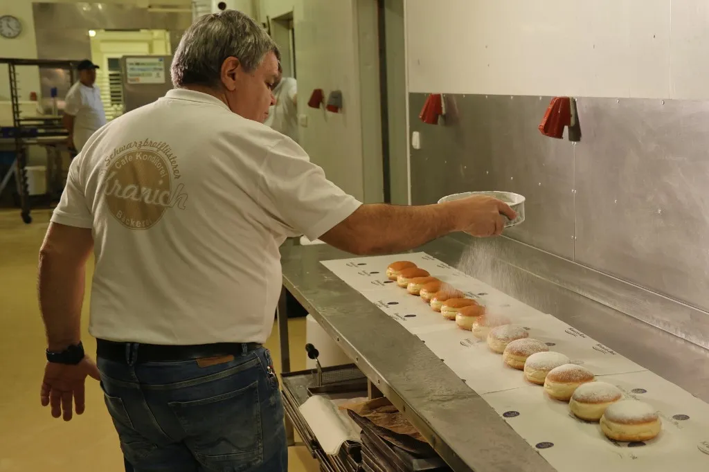 Kurt Kranich staubt in der Backstube frische Krapfen mit Staubzucker