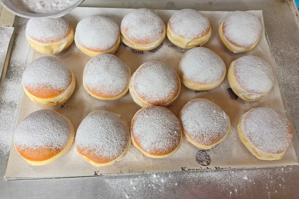 Frisch gefüllte Krapfen auf einem Blech mit Staubzucker